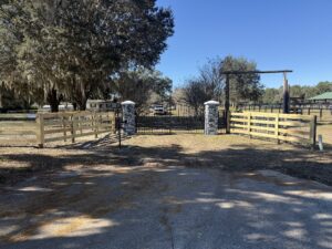 farm entrance with double wooden gate and 4 board fence along driveway